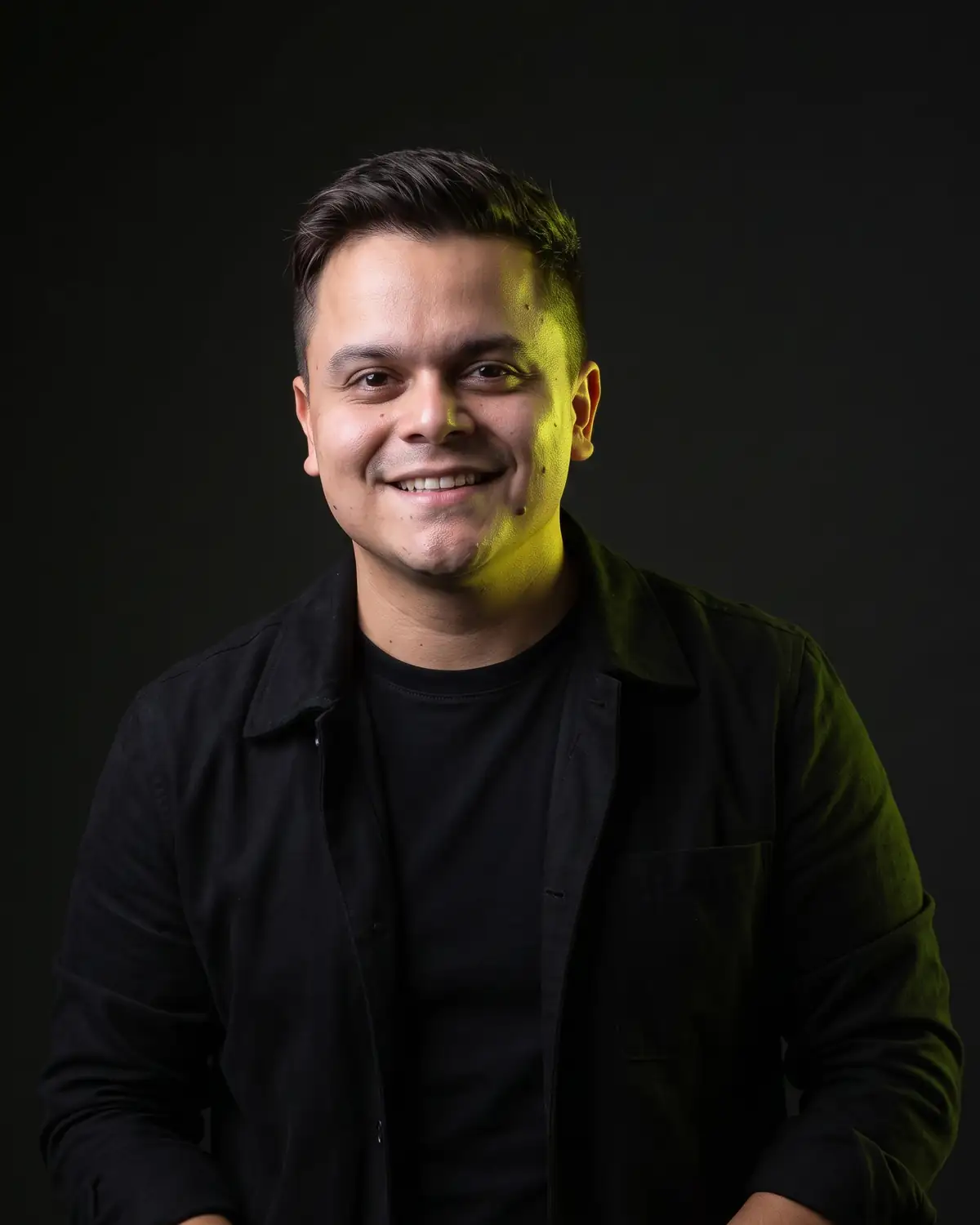 Israel Silva sonriendo, retrato de estudio con fondo oscuro